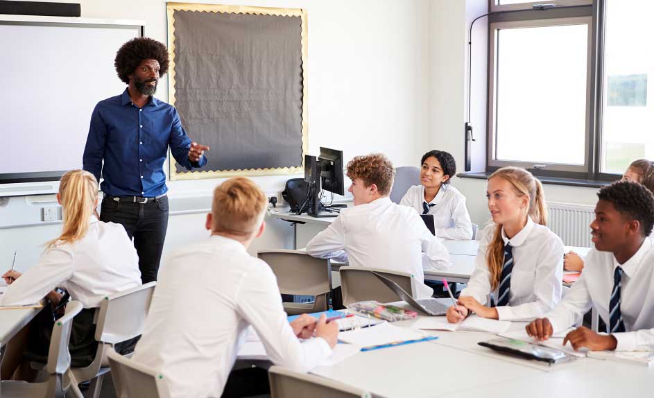 Secondary school children sat at tables with teacher leading a lesson